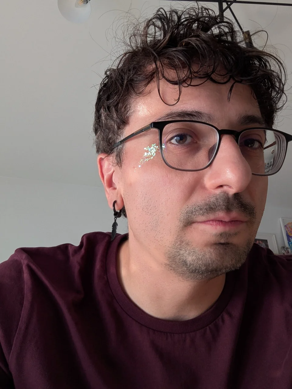 Serdar Kar mit Brille und bordeauxfarbenem Shirt, Glitzer unter dem Auge.